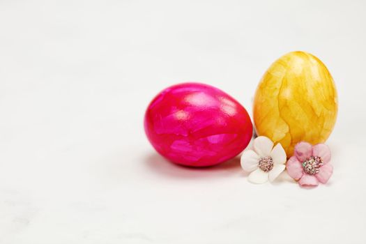 Easter eggs painted in pastel colors on a white background with copy space and cute spring flowers, Happy Easter Holiday concept with space for text. Yellow pink and blue bright colors