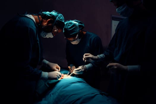 Surgical team performing surgery to patient in sterile operating room. In a surgery room lit by a lamp, a professional and confident surgical team provides medical care to an unconscious patient.