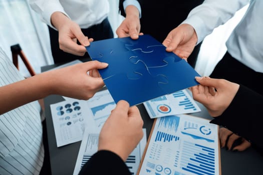 Closeup top view business team of office worker putting jigsaw puzzle together over table filled with financial report paper in workplace with manager to promote harmony concept in meeting room.