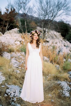 Smiling bride in a multi-colored wreath stands on a mountain among the stones. High quality photo