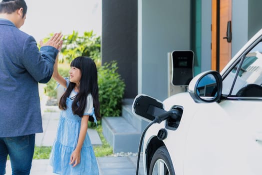 Progressive father and daughter returned from school in electric vehicle that is being charged at home. Electric vehicle driven by renewable clean energy. Home charging station concept for environment