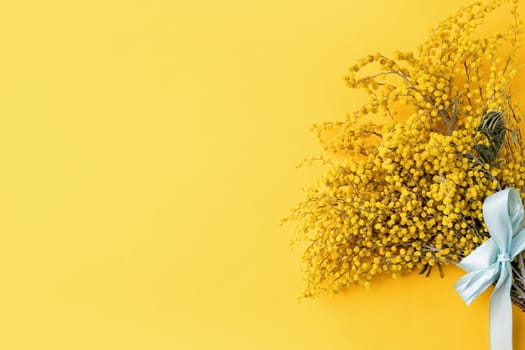 Frame of yellow mimosa flowers bouquet on yellow solid bakground. Spring concept. Flat lay. Top view, banner