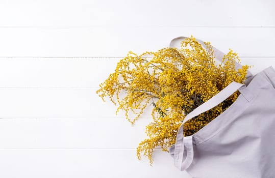 Frame of yellow mimosa flowers in shopping bag bouquet on wooden solid bakground. Spring concept. Flat lay. Top view, banner