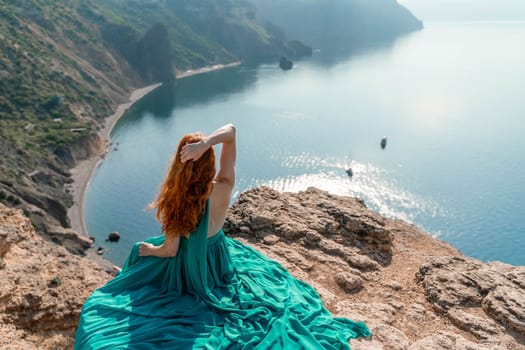 Woman sea. A happy girl is sitting with her back to the viewer in a mint dress on top of a mountain against the background of the ocean and rocks in the sea