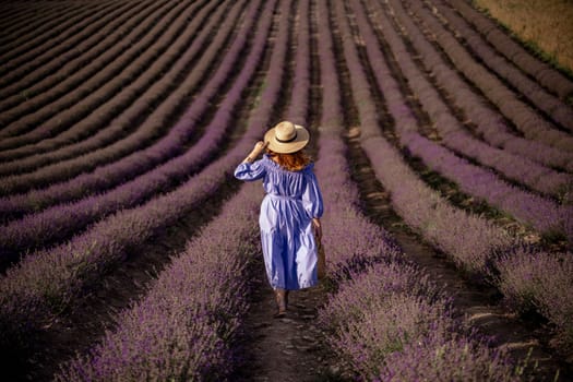Lavender is a woman. A happy middle-aged woman, in a blue dress and hat, walks through a lavender field.
