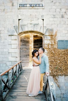 Groom hugs and kisses bride on the forehead on the bridge near Fort Mamula. High quality photo