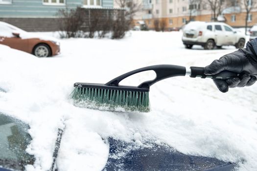 A man's hand in a black leather glove brushes the hood of his car after a snowfall in winter. Selective focus.