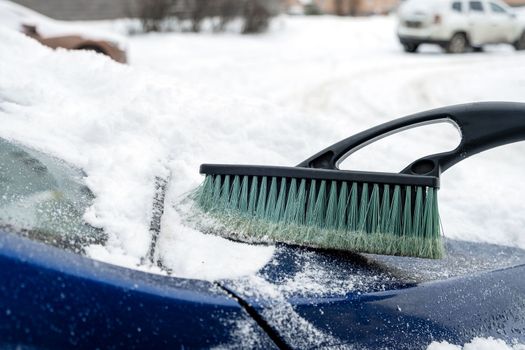 The hood of a car is cleaned with a brush after a snowfall in winter. Selective focus.