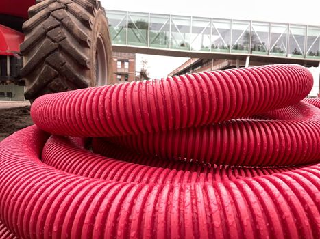 Red plastic corrugated pipes on the background of a building under construction and a tractor. Industrial zone, magenta color of the year, High quality photo