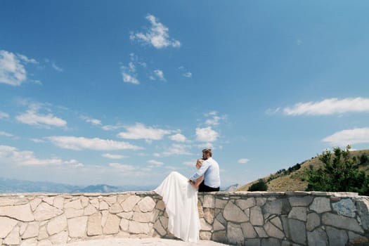 Bride and groom sit hugging on the observation deck. High quality photo