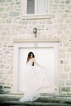 Bride holds the hem of her dress near the old stone building. High quality photo