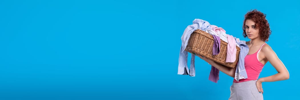 A woman with an angry face carries a wicker basket with shirts for washing. Daily household chores. Young attractive girl with curly hair.