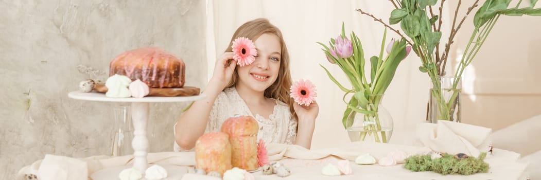 A girl with long hair in a light dress is sitting at the Easter table with cakes, spring flowers and quail eggs. Happy Easter celebration