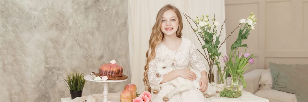 A girl with long hair in a light dress is sitting at the Easter table with cakes, spring flowers and quail eggs. Happy Easter celebration