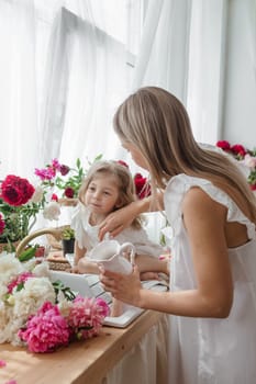 A little blonde girl with her mom on a kitchen countertop decorated with peonies. The concept of the relationship between mother and daughter. Spring atmosphere.