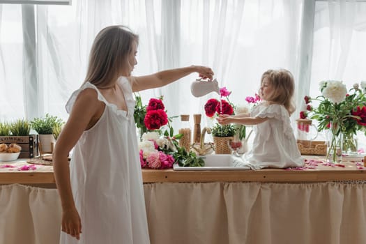 A little blonde girl with her mom on a kitchen countertop decorated with peonies. The concept of the relationship between mother and daughter. Spring atmosphere.