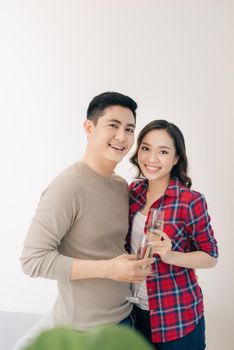 Cheerful couple celebrating their new house with champagne, standing by the window.