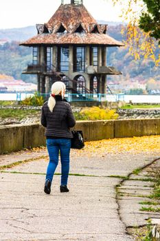 Alone woman walking on the autumn alley. Autumn landscape, orange foliage in a park in Orsova, Romania, 2020