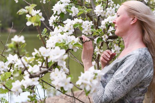 middel aged woman stands in the park next to a flowering tree, Spring time, Adult with blond hair, Wellness concept. High quality photo