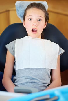 In the dreaded dentists chair...a young girl looking terrified while sitting in a dentists chair