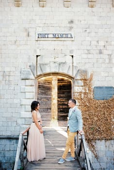 Bride and groom stand opposite each other on a wooden bridge to the entrance to Mamula Fort. High quality photo