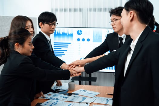 Closeup business team of suit-clad businessmen and women join hand stack together and form circle. Colleague collaborate and work together to promote harmony and teamwork concept in office workplace.