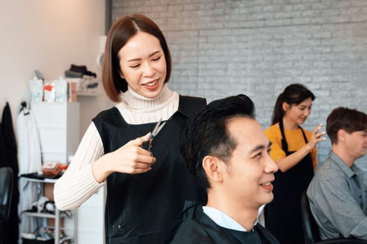 Asian female hairdresser making haircut for two male customer with male hairstyle in qualified barbershop. Men's hairstyling by a scissor and comb in hair salon concept.