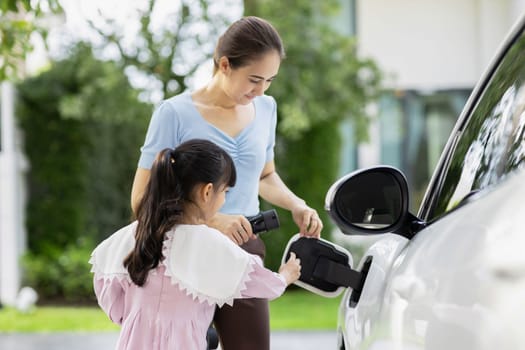 Progressive lifestyle of mother and daughter who have just returned from school in an electric vehicle that is being charged at home. Electric vehicle powered by sustainable clean energy.