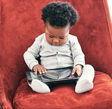Hes a curious fella. a little baby boy sitting in a chair holding a digital tablet