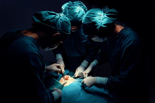 Surgical team performing surgery to patient in sterile operating room. In a surgery room lit by a lamp, a professional and confident surgical team provides medical care to an unconscious patient.