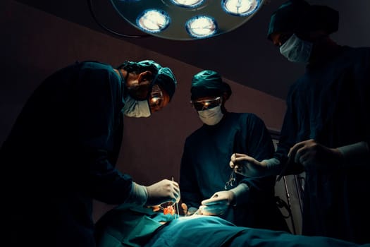 Surgical team performing surgery to patient in sterile operating room. In a surgery room lit by a lamp, a professional and confident surgical team provides medical care to an unconscious patient.