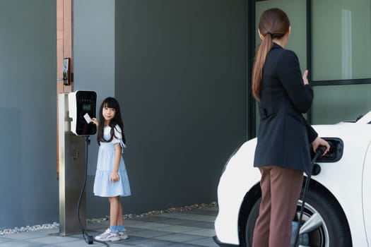 Progressive lifestyle of mother and daughter who have just returned from school in an electric vehicle that is being charged at home. Electric vehicle powered by sustainable clean energy.