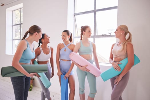 Friends talking before yoga class. Young women standing a pilates studio. Dedicated friends bonding before yoga class. Women waiting before holistic yoga class. Happy friends talking in yoga class.