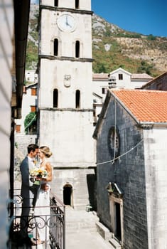 Groom hugs the smiling bride on the balcony near the ancient bell tower. High quality photo