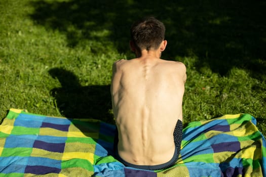 Guy with bare back on beach. Man is resting in park. Hot day in summer. Man's bare back.