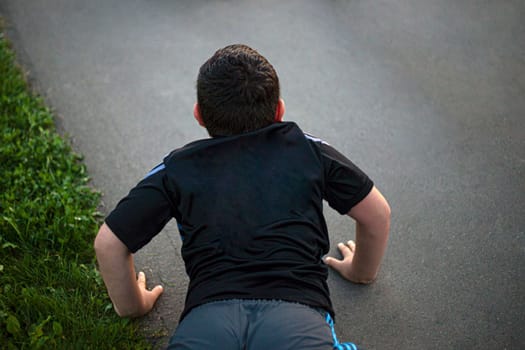 Child does push-ups from ground, Playing sports. Falling on asphalt. Boy is lying down.