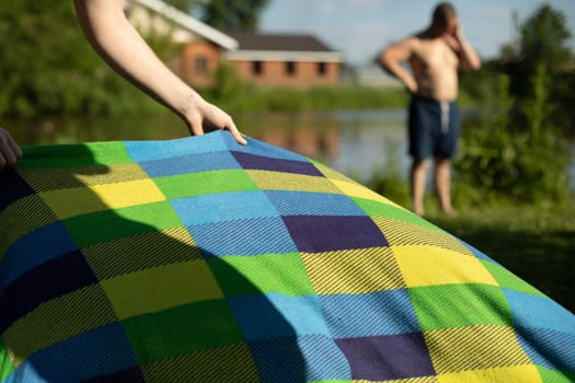 Relax in summer on beach. Colored blanket on lake. Details of picnic in park. Fabric with linear pattern.