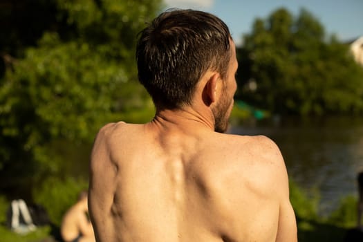 Guy's back in summer. Man's bare back on hot day. Middle-aged man on beach. Rest in heat.