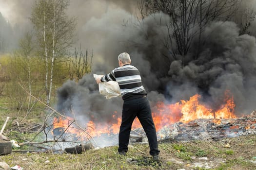 Man extinguishes fire on his own. Man and Fire. Civilian is fighting flames. Burning garbage in illegal landfill. Activist fights smoke.