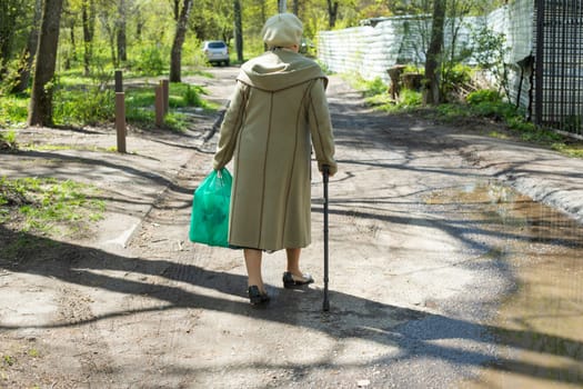 Pensioner walks down street. Grandmother in Russia. Woman with walking stick. Elderly man in town.