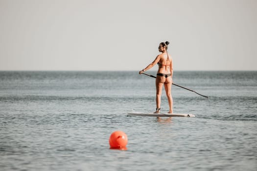 Sea woman sup. Silhouette of happy middle aged woman in rainbow bikini, surfing on SUP board, confident paddling through water surface. Idyllic sunset. Active lifestyle at sea or river