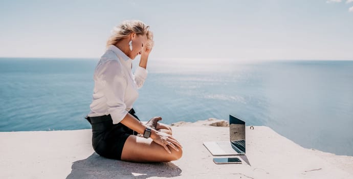 Happy girl doing yoga with laptop working at the beach. beautiful and calm business woman sitting with a laptop in a summer cafe in the lotus position meditating and relaxing. freelance girl remote work beach paradise