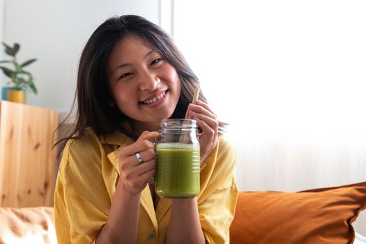 Happy teen asian girl showing healthy green juice looking at camera. Copy space. Copy space. Healthy lifestyle concept.