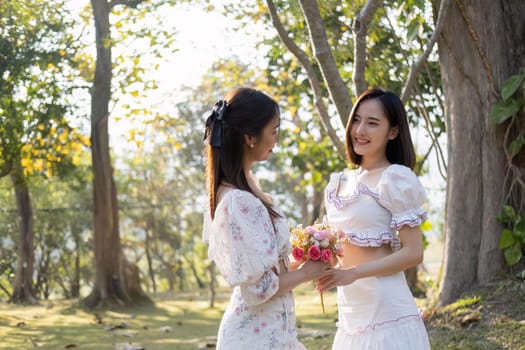 Attractive Asian woman giving a beautiful flower bouquet to her friend, in the park.