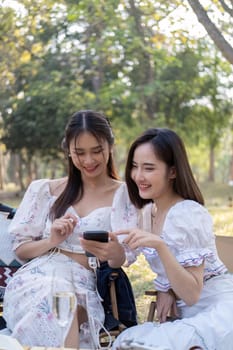 Relaxed Asian women in beautiful dresses are watching a video on a mobile phone togetherthey are having picnic,they talk happily.