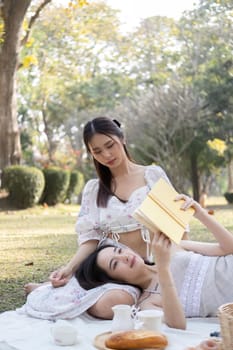 Two young Asian women beautiful read a book while picnicking in the beautiful garden together on the weekend.
