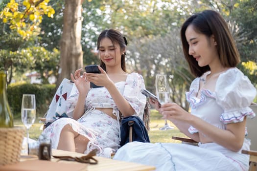 Asian women sit on picnic chairs, focusing on using their smartphones asian woman friends, they are having picnic,they talk happily.
