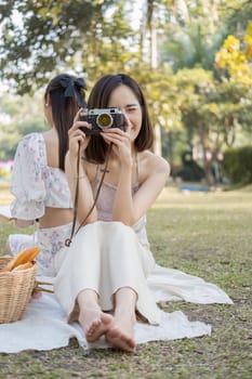 beautiful pretty Asian woman in casual clothes sits on picnic clothe, holding a camera, smiling and looking in the camera.