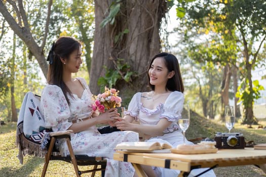 Gorgeous Asian woman giving a beautiful roses bouquet to her friend, having a special moment together in the park. female couple, lesbian, best friend, besties.