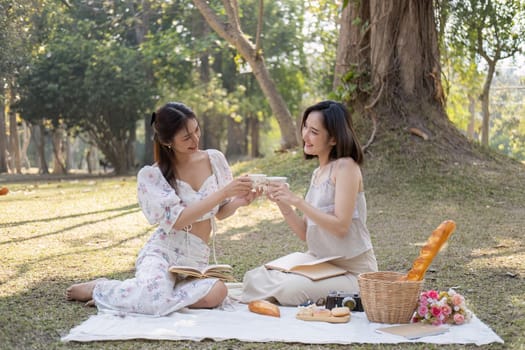 Two attractive and charming Asian women are enjoying an tea picnic in the beautiful park, sipping tea and spending the weekend together.
